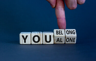 You alone or belong symbol. Businessman turns cubes and changes words you alone to you belong. Beautiful grey background. Business, psychology and you alone or belong concept. Copy space.