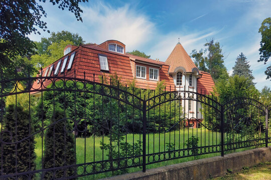Cozy rural mansion with courtyard landscaped by topiary ornamental plants and green grass lawn behind the fence in Kaliningrad, Russia (formerly Koenigsberg) at summer day