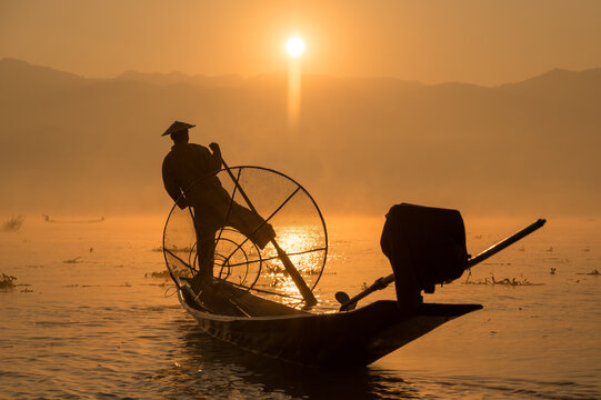 INTHA FISHERMEN, INLE LAKE, SHAN STATE, MYANMAR - 18 January 2020: Traditional fishing technique rowing with one-leg and using a conical net at sunrise.
