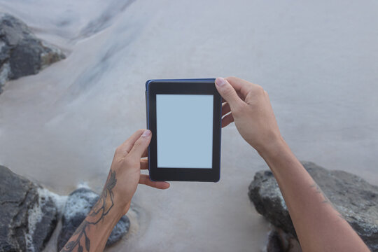 Male hands holding an tablet, e-book, on a rocky beach.Blank space on the tablet for mockup.