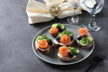 Sandwiches with salmon, cucumber, cream cheese and black olives on gray background. Homemade holiday snack.