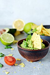 Bowl of guacamole dip with corn  nachos (chips) and ingredients on a blue background, selective focus. Mexican national dish.