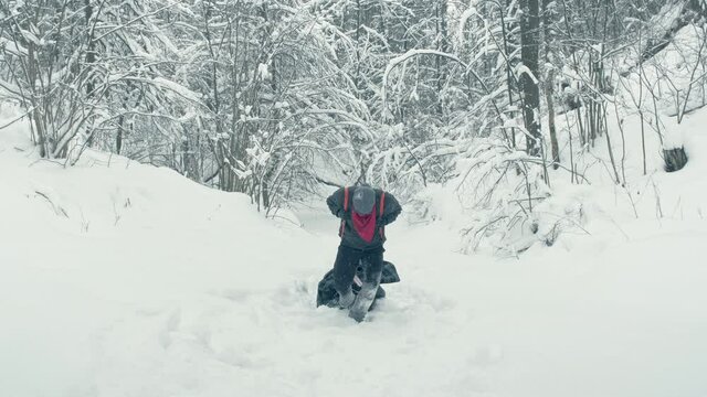 Man wearing a red bandana and black glasses drags a makeshift stretcher carrying a wounded man through a snowy area. Concept of rescue and survival