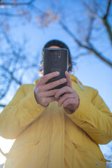 Young woman in yellow coat consults her phone to use her electric skateboard.