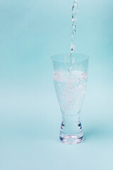 A jet of water fills transparent glass against a blue background.