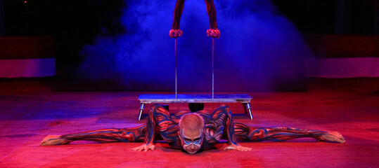 twins acrobats in neon costumes stand on their arms, ultraviolet makeup