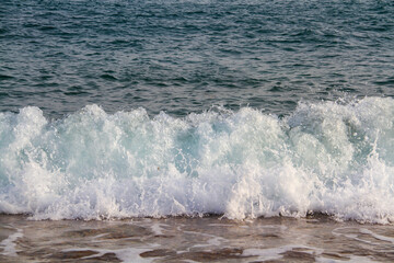 A sea wave with white foam runs on the sandy shore