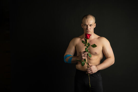 Athletic man holding a red rose, naked for the day of velentin pumped up, on his arm a teip of a bodybuilder romantic. lover guy LGBT. In the studio on a black background Smiling with tender lips