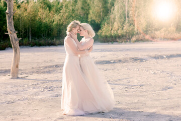 Fototapeta na wymiar Two brides women in white dress with blonde hair hugging each other
