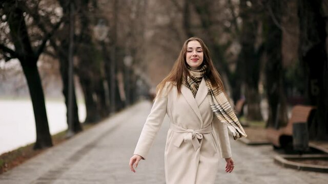 Young beautiful woman in a white coat spinning in the city park. Attractive fashion model with flying hair. Natural Beauty with Freckles. Beautiful girl woman shakes hair. Slow motion