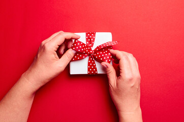 Hands tie a bow on gift box over red background