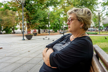 Mature sad woman is resting in the old city park.