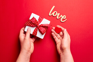 Hands holding gift box with small heart over red background