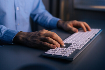 Close-up hands of unrecognizable man writing message to social network. Closeup view of developing programming and coding on wireless keyboard late night working. Concept of remote working.