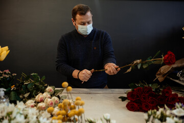 Happy caucasian florist making bouquets of red and pink roses for valentine's day. Concept of human emotions, facial expression, love, and hard work in this pandemic times.