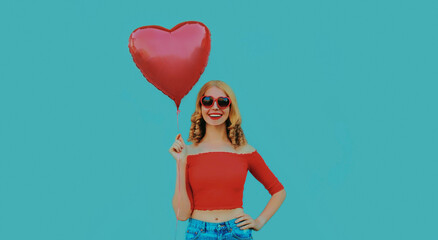 Portrait of cute smiling woman with red heart shaped balloon on a blue background