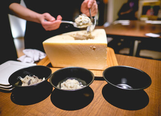 Woman serving a gourmet cheese preparation in black pottery in a wooden table at restaurant, Japan