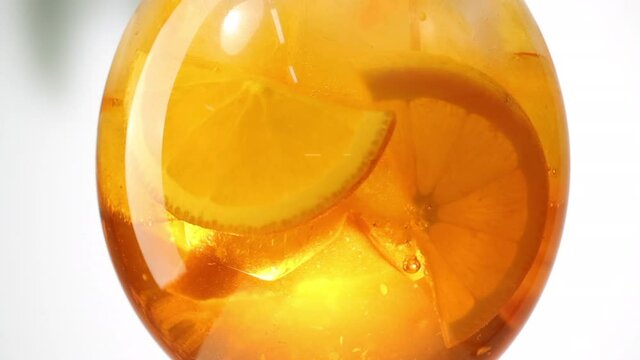 slow motion close up of turning orange aperol spritz cocktail glass with ice cubes and fruit slices