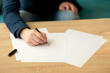 Businessman in the office writes a letter or signs a document on a piece of white paper with a fountain pen with nib. Closeup of hands of a businessman in a suit