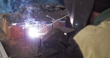 Close-up blacksmith welder in protective mask works with metal using a welding machine, bright sparks and flashes in super slow motion