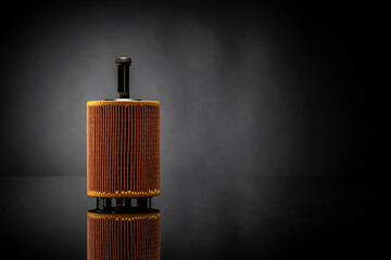 Car OIL filter used for car maintenance placed on black reflexive glass isolated on black background on the left side with negative space on the right. 