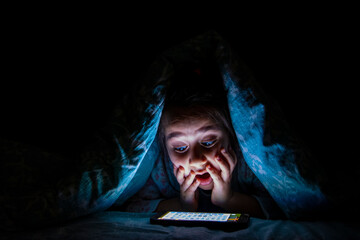 Little girl is surprised to see the phone screen in bed in the dark