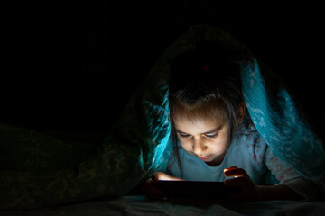 Little girl is using phone in bed in the dark