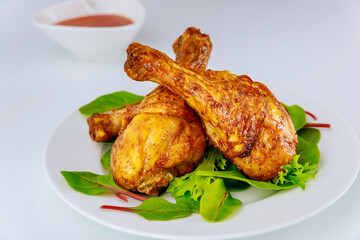 Roasted spicy chicken drumsticks with salad on white background.