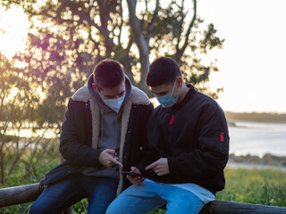 Amigos sentados durante la puesta de sol hablando y mirando su teléfono móvil
