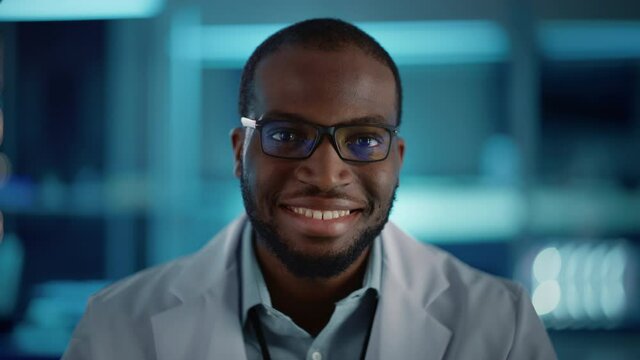 Handsome Black Man Wearing Glasses Smiling Charmingly Looking at Camera. Young Intelligent Male Engineer or Scientist Working in Laboratory. Technological Bokeh Blue Background. Close-up Shot