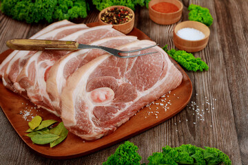 Sliced raw pork shoulder with spices on wooden board.