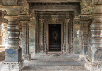 Lakkundi, Karnataka, India - November 6, 2013: Brahma Jinalaya temple. Doorway from Mandapam into sanctum has highly sculpted frame. Sculpted pillars in front. Idol far in back.