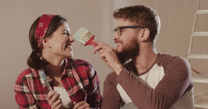 Portrait of young happy married couple at home during renovation. Beautiful caucasian woman and man smear each other with paint.