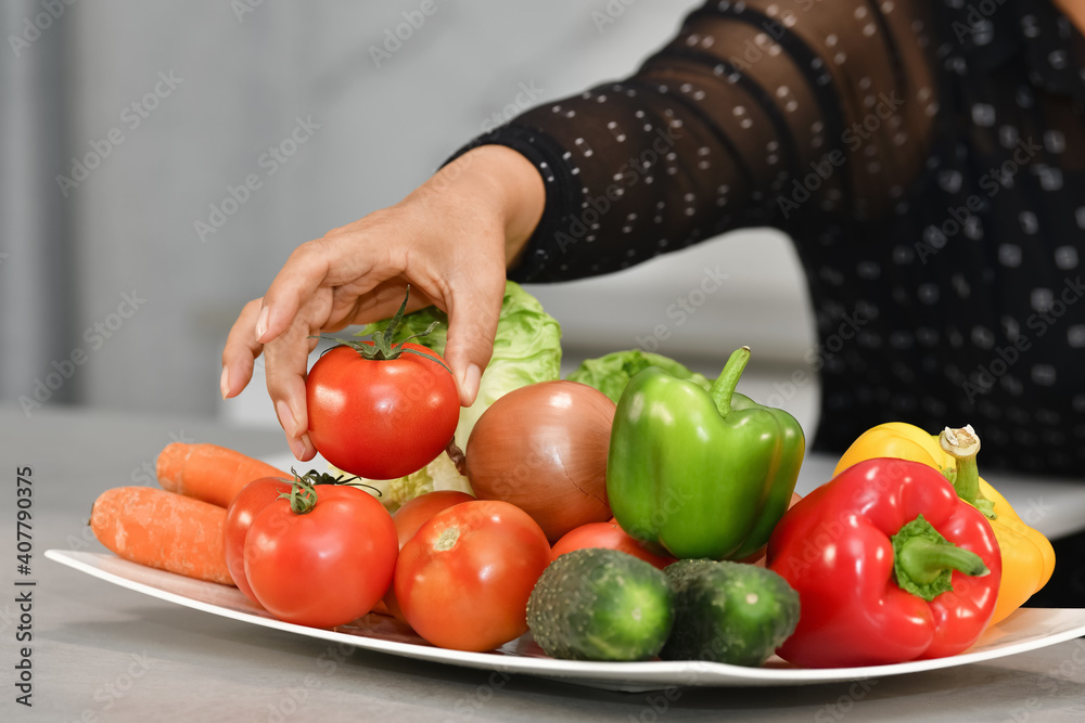 Wall mural Selective focus shot of a female's hand taking a tomato from a plate with fresh vegetables