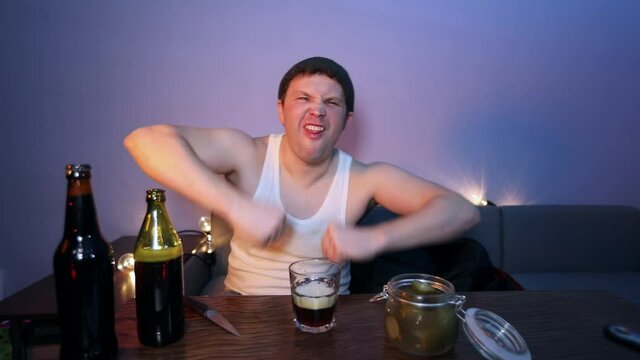The man drinks beer, eats sausages with cucumber and listens to music