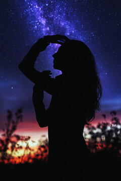 Woman posing nicely, observing the universe against the backdrop of the shining Milky Way galaxy and a beautiful sunset. Silhouette of a woman against the background of blurry stars