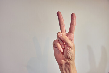 A hand with a victory sign on a light background.