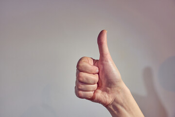 A hand with a thumb up on a light background.