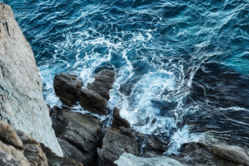 Stormy sea with rough white waves and stony sea beach view from above. Close-up photo of a rocky shore with gloomy sea waves