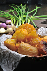 Fried cassava with garlic, onion and green onion garnish on a wooden cutting board