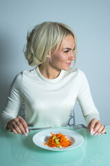 Girl at the table in the kitchen eats a healthy and tasty salad with carrots. The girl has a healthy breakfast in the kitchen. 