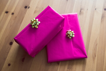 couple of birthday present wrapped up in pink and gold on wooden table, concept of parties and celebrations