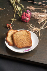 two slices of banana bread on a small plate with a wooden chopping board and garnish with flowers and straw