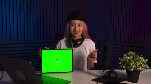 Asian zoomer girl emotionally recommended application on smartphone and tab. Chromakey on the screen of the tablet. Content generation room. Girl in white shirt and black hat. Girl with pink hair