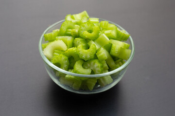 Celery slices in glass bowl on dark background.