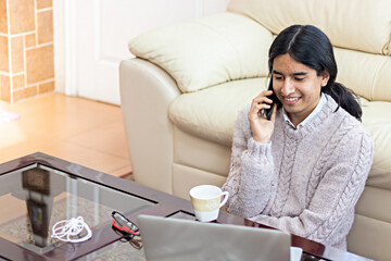 young man working from home, talking on the phone while watching a computer