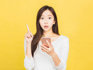 shocked young woman holding mobile phone and pointing to copy space