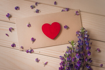 flat lay red wooden heart lies on craft envelope on rustic table with bouquet of flowers lupine