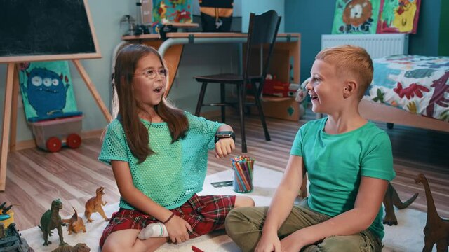 Little girl with brother activating smartwatch futuristic application browsing software virtual network choosing games and objects on holographic screen. Excited kids. Children and technologies