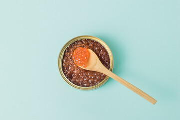 Wooden spoon in a jar with red caviar on a blue background.